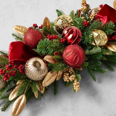 Celebrate the beauty of the holiday season with our 'Twas the Night collection featuring festive pieces in a coordinating color palette of red, gold, cream-white and green. A showy display for the dining table or entryway console, this centerpiece is resplendent with gleaming ornaments and velvet ribbon nestled amongst preserved and faux foliage. Hand-assembled of faux pine needles, berries, painted plastic and polyester; natural twig and wire base. Pre-strung with 70 warm white lights. Battery Red And Gold Christmas Centerpiece, Holiday Floral Arrangements Christmas, Christmas Wreath Centerpieces For Table, Long Table Christmas Centerpieces, Console Table Christmas Decor Ideas, Christmas Entry Table Decor, Christmas Floral Centerpieces, Christmas Table Wreath, Christmas Centerpieces For Table