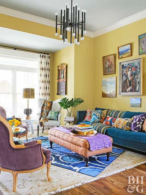 Yellow is one of many colors featured in this eclectic living room. The yellow walls host a gallery of colorful art, and a pacific blue sofa holds plenty of patterned pillows. Layered rugs soften the space, while yellow living room accessories, like fresh flowers, a lampshade, and throw pillows, incorporate the sunny color scheme throughout. Yellow Living Room Accessories, Yellow Walls Living Room, Yellow Decor Living Room, Yellow Wall Decor, Furnitur Ruang Keluarga, Yellow Room, Yellow Living Room, Living Room Color Schemes, 카페 인테리어 디자인