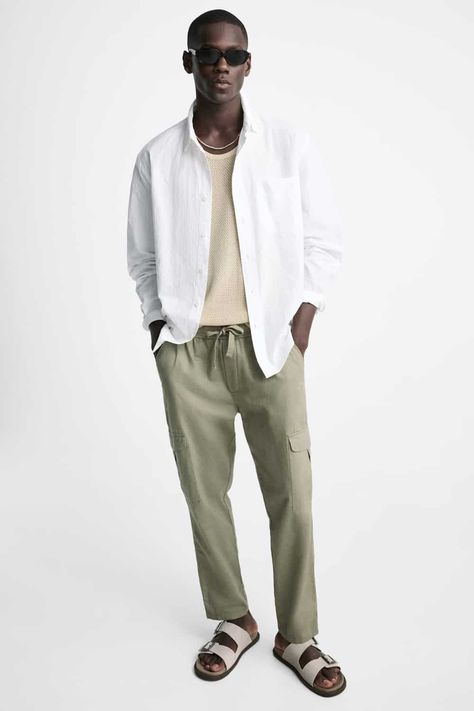 Men's green cargo pants, knit cream T-shirt, open white shirt and stone sandals outfit. This outfit was included in the article: What Colours To Wear With Green Pants: 7 Foolproof Shirt Options, on MensFlair.com Light Green Pants Outfit Men, Olive Green Pants Men, Colored Pants Outfits, Green Pants Men, Outfit Pria, Green Khaki Pants, Green Pants Outfit, Green Chino Pants, White Shirt Outfits