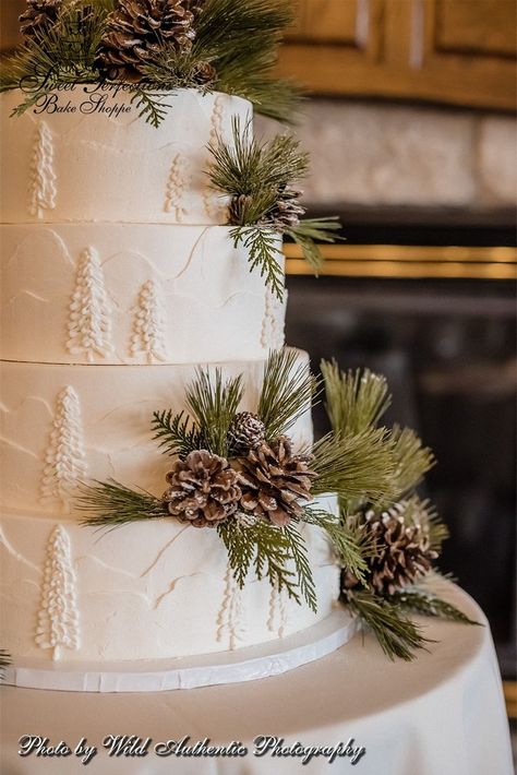 For Becky and Joshua’s outdoorsy February wedding, we topped their four-tier cake with a burst of pinecones and evergreen dusted with powdered sugar, which looks like a fresh layer of snow. Simple yet effective! The rustic motif continues down the side of the cake, which is frosted in buttercream textured to look like snow-covered mountains and trees. An elegant idea for a woodland, Christmas, or Winter Wonderland themed wedding. Photo from www.thewildauthentic.com. #spbakeshoppe Rustic Christmas Cake Decorating Ideas, Buttercream Texture Wedding Cake, Wedding Cake With Pinecones, Pine Cone Wedding Cake, Rustic Christmas Wedding Cake, Pinecone Wedding Cake, Winter Wedding Cakes Rustic, White Winter Wedding Cake, Evergreen Baby Shower Theme