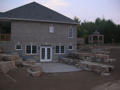 Walkout basement with limestone tiered retaining walls, this is similar to how the west side of our home will look like when removing the hillside and opening it up to a walkout with a deck above. Walkout Basement Patio, Basement Window Replacement, Rock Steps, Basement Entrance, Basement Doors, Concrete Retaining Walls, Basement Layout, Stone Retaining Wall, Landscaping Retaining Walls