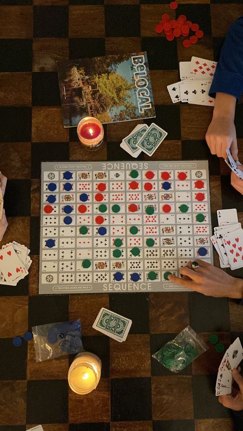 top-down overhead photo of sequence (the board game) splayed across a black and brown wooden coffee table as three people are playing the game, two candles are lit on the table Cabin Aesthetic With Friends, Checkers Game Aesthetic, Cabin Weekend Activities, Family Board Games Aesthetic, 30th Birthday Cabin Weekend, Cozy Cabin Vibes, Board Game Coffee Table, Cabin Party Aesthetic, Aesthetic Board Games