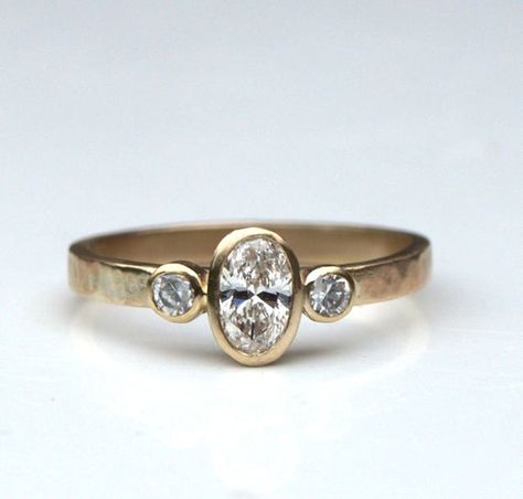 A lovely oval diamond trilogy ring. This one was made in recycled 9ct yellow gold but you can have any metal, just ask for a quote. ( Yellow and white gold are recycled, platinum isn't at present). The band has a textured finish but can also be smooth. The lovely central diamond is  6x 4mm oval, 0.37ct, flanked by two 2mm round diamonds (0.035ct each). The setting allow another ring to sit flush against this one and the low height makes it very practical. The band is 2mm wide.The ring is made to Wide Band Oval Engagement Ring, Flush Setting Engagement Ring, Three Stone Bezel Engagement Rings, Compulsory Heterosexuality, Low Setting Engagement Ring, Flush Ring, Diamond Trilogy Ring, Infinity Diamond Ring, Ring Inspiration