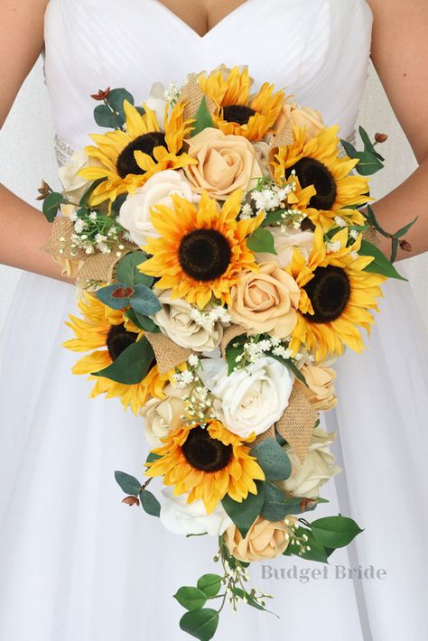 This striking cascading brides’ bouquet is made with an elegant combination of beige, champagne, and sunflowers to create a beautiful amount of depth and contrast within this bouquet. The sunflowers and roses alongside the variety of mixed foliage and filler make this bouquet a stand out. As always, our bouquets are wonderful for those who are allergic to flowers and pollen, and have the added bonus of not attracting any bees or bugs. All of our bouquets are wired by hand, so that you can rest a Western Wedding Bouquets With Sunflowers, Bride Bouquets Sunflowers, Sun Flower Wedding Theme Bridesmaid Dresses, Sunflower Hydrangea Bouquet, Summer Sunflower Bouquet, Rose And Sunflower Wedding Theme, White Sunflower Bouquet, Sunflower Bouquet Aesthetic, Sunflower Bouquet Wedding