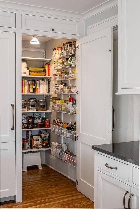 A white paneled cabinet doors opens to reveal a hidden kitchen pantry equipped with stacked white metal spice baskets mounted on a gray wall adjacent to white modular shelves. Kitchen Pantry Doors, Organiser Cucina, Open Pantry, Wooden Kitchen Cabinets, Hidden Pantry, Desain Pantry, Fancy Kitchens, Hidden Kitchen, Pantry Shelving