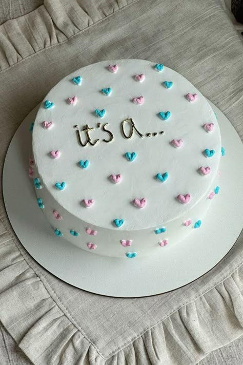 A gender reveal cake with white frosting and pink and blue hearts, with the text "It’s a..." written on top. Simple Reveal Ideas, Gender Reveal Lunchbox Cake, Gender Reveal Cake Sayings, Gender Reveal Cutout Cookies, Easy Cute Gender Reveal Ideas, Cheesecake Gender Reveal, Dessert For Gender Reveal Party, Minimal Gender Reveal Cake, Gender Reveal Cake Homemade