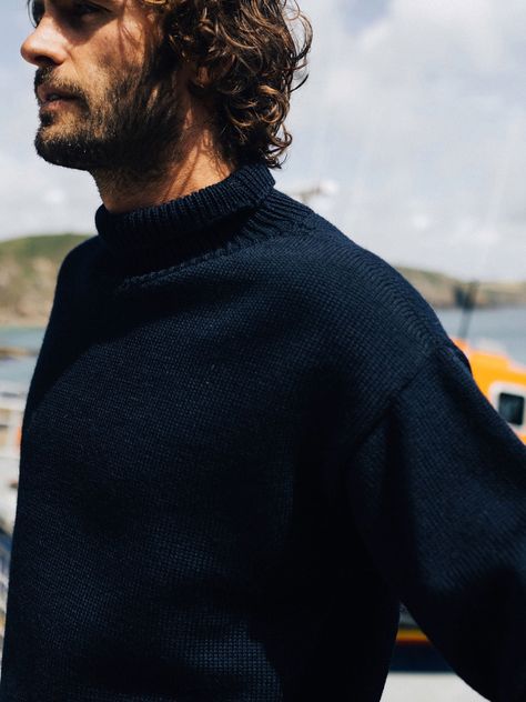 The men's navy RNLI Cromarty Jumper has been modelled on classic seafarers' jumpers, made in England with 100% British wool to retain utmost authenticity. Tightly knitted and featuring a chunky low-line roll-neck collar to keep out sea spray and wind, these traditional knitted jumpers have long kept seafarers warm and protected in rough seas. 10% of every sale from the collection will go to support the vital work of the RNLI. Roll Neck Sweater Outfit, Jumper Outfit Men, Mens Roll Neck Sweater, Knitted Jumper Outfit, Wool Clothes, Knitting Things, Navy Jumper, Rough Seas, Jumper Style