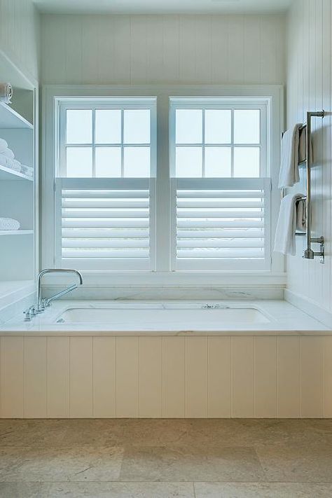 A drop-in bathtub fitted with a white shiplap trim boasts a marble deck holding a polished nickel deck mount tub filler in front of white built-in shelves. Drop In Tub Ideas, Bathtub Tile Surround, Shiplap Trim, White Herringbone Tile, Acrylic Vanity, Bathtub Shower Combo, Built In Bathtub, Marble Tub, Built In Bath