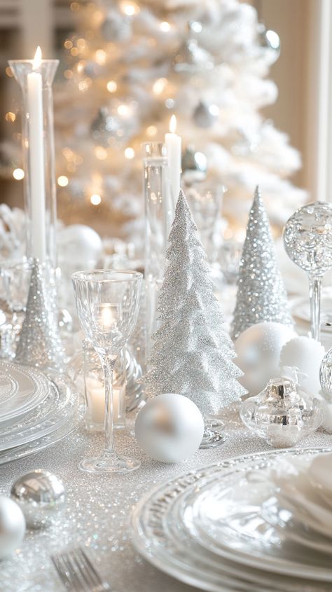 Elegant white and silver Christmas table setting with crystal glasses, candles, and glass tree figurines in a modern design. White And Silver Christmas Table Setting, New Years Dining Table Decor, All White Christmas Party Decorations, White Christmas Dinner Party, White And Silver Table Settings, Silver And White Christmas Table Decor, Snowy Tablescape, Snow Tablescape, Silver Christmas Table Settings