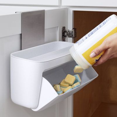 DoorStash Dishwasher Pod Holder adds some pep to your dishwashing steps. It elevates pods from the cabinet floor to an accessible, over-door location. A large bin rotates open so you can quickly grab a pod and move on. The top tray offers an extra storage spot. With pods in place, running the dishwasher feels like a power play. | YouCopia® DoorStash Dishwasher Pod Holder 10.1 x 11.8 x 6.1 in, Plastic | Organization | ZSNR1077 | Wayfair Canada Dishwasher Pods Storage, Home Storage Hacks, Kitchen Sink Organizers, Laundry Detergent Container, Detergent Storage, Detergent Container, Dishwasher Pods, Laundry Pods, Closet Renovation