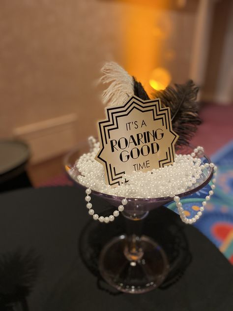 Giant Martini Glass Centerpiece for popular Roaring 20s party filled with beads, feathers & cute signage. #Roaring20sdecor #roaring20scenterpieces 20s Themed Centerpieces, Gatsby Party Centerpieces Diy, The Great Gatsby Party Invitations, Roaring 20s Party Centerpieces, Roaring 20s Graduation Party, Gatsby Centerpiece Ideas Roaring 20s, Roaring 20s Centerpieces Diy, Roaring 60s Party, Roaring 20s Table Decor