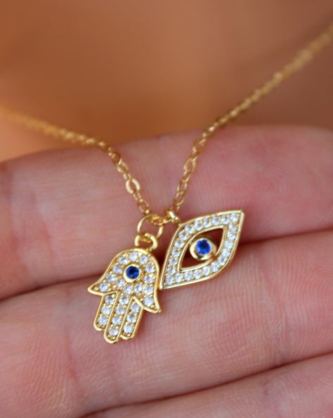 "This is a gorgeous little gold filled evil eye hamsa double charm necklace. These sparkling little charms come together on a shiny 14kt gold filled cable chain. Both charms are 14kt gold filled, have a small clear pave crystals with a blue center crystal. Hamsa measures 15x11mm and evil eye 15x8mm. PLEASE CHOSE YOUR LENGTH. These charms are even prettier in person! Comes in a cute gift box! Model is wearing a 16\" length in photo. This listing is for the double pendant necklace only. Shown with Gold Evil Eye Necklace, Hamsa Necklace Gold, Floral Henna, Evil Eye Hamsa, Hamsa Jewelry, Evil Eye Necklace Gold, Gold Hamsa, Hamsa Necklace, Jewelry Accessories Ideas