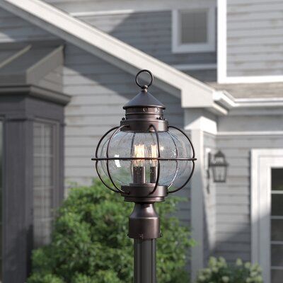 It’s hard to beat the feeling of coming home after a long day. Make that moment even sweeter by casting a warm and welcoming glow over your outdoor space with this three-light post lantern. Crafted of metal in an oil-rubbed bronze finish, this antique-inspired design showcases a classic silhouette with an open and wiry cage topped off with a slanted roof and a ring finial. A clear seeded glass shade completes the look with a hint of vintage appeal. Size: Large | Three Posts™ Smithboro Oil Rubbed Oil Rubbed Bronze Lighting, Light Posts, Slanted Roof, Coastal Lamp, Country Lighting, Driveway Lighting, Post Lanterns, Lantern Head, Light Post