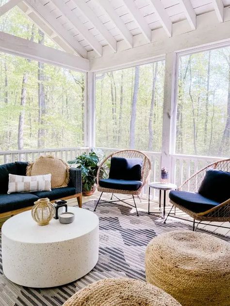 a modern boho screened porch with a navy sofa, rattan chairs, jute poufs, a coffee table and some potted greenery Screened In Porch Living Room, Screened In Patio Inspiration, Screened Patio Furniture Ideas, Enclosed Patio Furniture Ideas, Screen Porch Furniture Ideas, Screened Porch Designs Modern, Furniture For Screened In Porch, Large Screened In Porch Decorating Ideas, Screened In Porch Inspiration