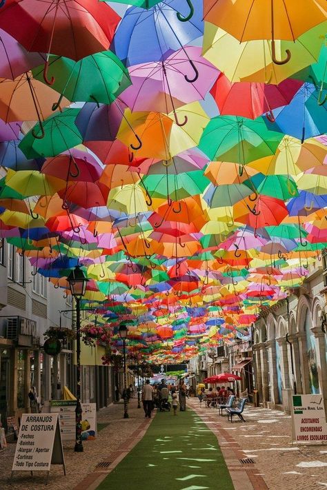 Águeda's Umbrella Sky Project began in 2011 as a part of the Portuguese city's annual Ágitagueda Art Festival. Each summer, when temperatures soar, a handful of Águeda's narrow streets feature canopies of colorful umbrellas that provide shade to the pedestrians below. Umbrella Street, Burning Men, Colorful Umbrellas, Venice Italy Travel, Beautiful Streets, Countries To Visit, Canopies, Kat Von D, Beautiful Places In The World