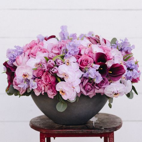 This bold new floral design is endlessly lush and sure to make them smile. Deep burgundy calla lilies, delicate lavender sweet peas, reflexed violet roses, perfectly ruffled pink roses, lavender tulips, and two-toned phalaenopsis orchids come together in perfect harmony to create a majestic lavender hued garden. Resting atop a 21" wide by 10" tall grey textured vase, and stands at approximately 21" tall overall. This design is available in smaller sizes; pease call for custom orders. Sweet Sangria, Lavender Tulips, Violet Roses, Roses Lavender, Pink And Purple Flowers, Phalaenopsis Orchid, Sweet Peas, Calla Lilies, Beautiful Bouquet Of Flowers