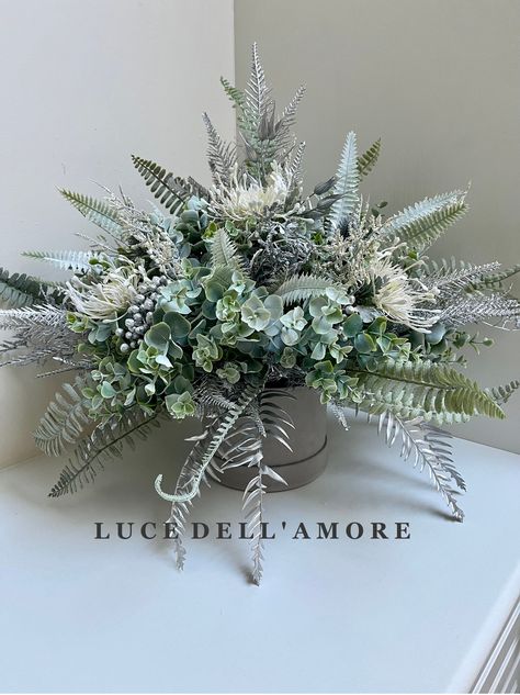 Winter Wonderland floral arrangement presented in a hat box .  A beautiful arrangement presented in a grey silver hat box, of sage and silver and white ferns, thistles and eucalyptus faux flowers, with protea and astilbe. Presented in a hat box colour of your choice. The box sizes available are: Small box 14.5wide x11cm high ( finished with arrangement 60cmx45cm) Medium box 17.5 wide x 12.5cm high (finished arrangement 70cmx 50cm) Large box 19.5 wide x 14cm high (finished arrangement 80cmx55cm) Winter Wonderland Floral Arrangements, Faux Winter Floral Arrangements, Dome Flower Arrangement, Winter Flower Arrangements, Winter Floral Arrangements, Silver Hat, Winter Florals, Christmas Planters, Christmas Floral Arrangements