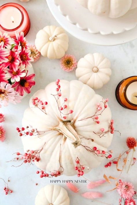 A festive fall arrangement featuring white pumpkins adorned with pink berries, surrounded by pink and red flowers, candles, and delicate leaves on a pale background. Pink Pumpkin Centerpieces, Pumpkin And Flowers, Pumpkin With Flowers, Fall Decor Kitchen, Pale Background, Pink And Red Flowers, Pink Berries, Fall Container Gardens, Pumpkin Vase