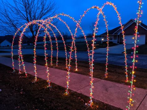 Decorate for christmas with PVC. I used 1/2" PVC to create this... Made 10 arches which is 2 bundles of 10ft PVC pipe (sched40). It is flexible enough to curve this much without needing any heat guns.  Bought 20 two foot 3/8 rebar and hammered it about 8 inches into the ground. Bought ten 1/2" couplings and some PVC cement (the pipe will pop out of the coupling if you dont use the cement ). Went to Menards and bought 20 boxes of Christmas lights that was 21ft per box for 2.99 each. Diy Christmas Driveway Arch, Pvc Arch Christmas, Christmas Lights Outside Pvc, Outdoor Christmas Arch, Diy Driveway Arch Christmas Lights, Pvc Pipe Christmas Decorations, Pvc Christmas Arch, Christmas Arches Outdoor, Pvc Christmas Tree