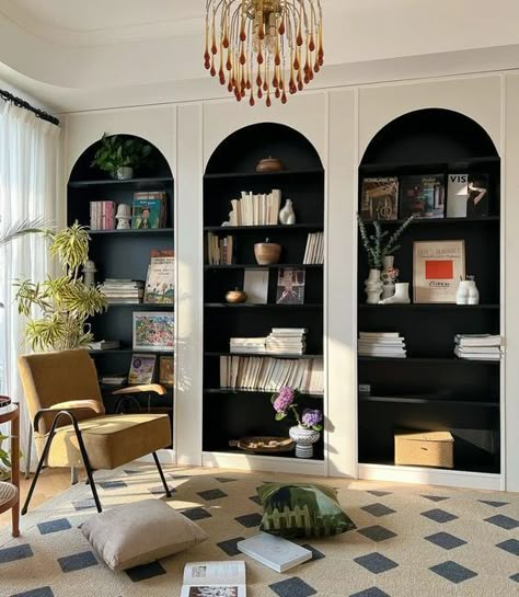 Picture of white arched bookcases with black backing and shelves, with amazing books and decor, a yellow chair and a rug for a reading nook Corner Shelves Built In, Arch Top Bookcase, Upstairs Reading Nook, Arched Bookcase Living Room, Arched Bookshelf Built Ins, Arch Bookshelf Built Ins, Arch Bookshelves, Arched Cabinet Living Room, Arched Library