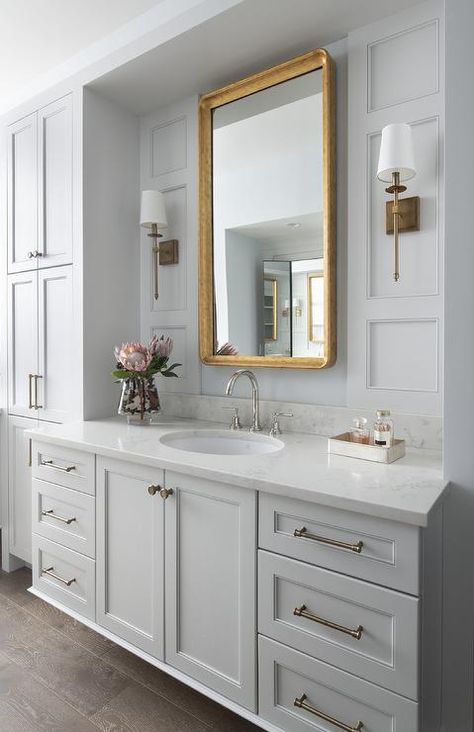 A curved gold leaf mirror hangs between aged brass sconces fixed to a light gray wall accented with light gray trim. Bathroom Features, Light Grey Walls, Transitional Bathroom, Master Bath Remodel, Mirror On The Wall, Home Luxury, Upstairs Bathrooms, Bathroom Redo, Girls Bathroom