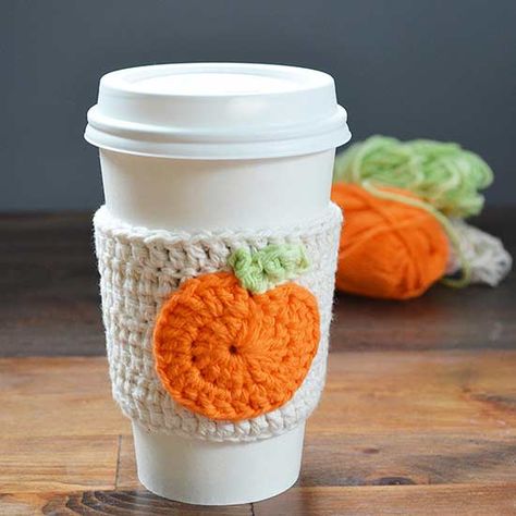 Embellish your favorite coffee cup with an adorable pumpkin cozy. Use the instructions linked at the bottom of this slide to crochet a sleeve to snuggly fit a cup or mug using beige cotton yarn. Next, make a pumpkin with orange and green yarn and attach the finished product to the sleeve using a needle and thread./ Coffee Cozy Pattern, Crochet Pour Halloween, Crochet Mug Cozy, Crochet Coffee Cozy, Pumpkin Applique, Crochet Cup Cozy, Fall Crochet Patterns, Coffee Cup Cozy, Confection Au Crochet