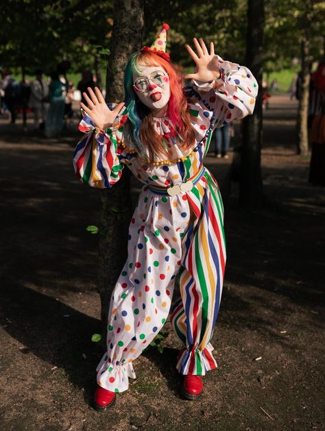 Girl in a white clown suit, half spotty, half stripey with primary colours. She has rainbow hair and a little hat and red shoes Make Your Own Clown Costume, Clowncore Halloween Costumes, Clown Outfit Reference, Clowncore Outfit Drawing, Clown Outfit Inspiration, Rainbow Clown Outfit, Cute Clown Outfit Aesthetic, Clown Aesthetic Costume, Jester Core Outfit