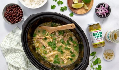 a slow cooker filled with Slow Cooker Chicken Chile Verde covered in cilantro, with beans, rice, lime, and onion in bowls off to the side and a jar of trader joe's salsa verde. Shortcut Recipes, Chicken Chile Verde, Chicken Chili Verde, Chicken Verde, Chicken Chile, Hispanic Dishes, Verde Chicken, Slow Cooker Chicken Chili, Salsa Verde Chicken