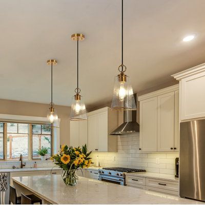 Doubling as a lighting source and fashioned decorative piece, this single pendant lighting fuses elegance and luxury. With a sleek design, the frame features a hammered glass embedded visual-delight texture, exuding an air of sophistication and luxury. The brim of the glass is painted with stain gold and the hardware is electroplated in an elegant brass finish that pairs well with the textured clear glass that strikes a harmonious balance of colors and textures. The lighting from one Type A bulb Farmhouse Pendant Lighting Dining Room, Over The Island Pendant Lights, Oil Rubbed Bronze And Gold Kitchen, Modern Pendant Lighting Kitchen Island Gold, Taj Mahal Quartzite Kitchen Island, Antique Kitchen Light Fixtures, Brass Pendant Lighting Over Kitchen Island, Transitional Kitchen Pendants, Lighting For Island Kitchen