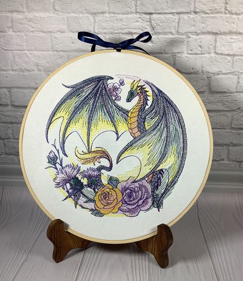 This floral dragon design is embroidered onto white colored cotton canvas and stretched into an 10 inch hoop.  There is a backing on the hoop.  Embroidery hoops are so easy to display.  You can use a plate display stand, or simply tap a hanging nail into the wall and slip the hoop over it. Pricing is determined by the stitch count.  Many of the designs are very detailed and can have over 60,000 stitches and some even more than that!  Please note that the designs are made to order, colors may vary slightly.  If you would like a different color ribbon,  specify in the personalization area. I have tons of designs, if you are interested in another subject or theme, contact me.  I would love to work with you to find the perfect home decoration or gift. Cute Dragon Embroidery, Dragon Embroidery Pattern, Watercolor Embroidery, Plate Display Stand, Floral Dragon, Plate Display Stands, Embroidery Decor, Embroidered Dragon, Dragon Embroidery