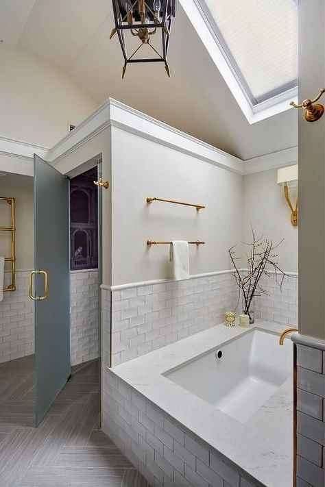 Vaulted ceiling in a master bathroom features a skylight over a bathtub nook fitted with white glazed stacked tiles, brass hardware, and a Ruhlmann Double Sconce. Luxury Spa Bathroom, Small Apartment Bathroom, Bathroom Interior Design Small, Gorgeous Bathroom, Hells Kitchen, Bathroom Trends, Apartment Bathroom, Bathroom Spa, Farmhouse Bathroom Decor