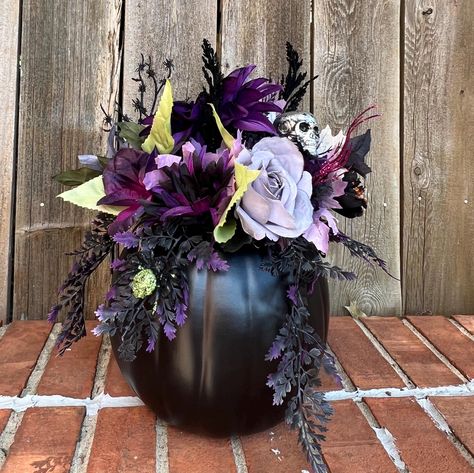 This  flower arrangement features all the things that make Halloween fun and  beautiful.  The black artificial pumpkin has the lid carved out and attached to the back of the arrangement.  The center is filled with flowers in the hues of gray, purple, black, and green.  Fun picks feature a silver skull, a purple and a green spider small spider web.  Black and purple feathery sprays and glittery berry sprays complete this arrangment   The pumpkin arrangement measures 15" in heigth and 12" at the widest part.   Item #FLR - 84 Halloween Flowers Bouquet, Spooky Flower Arrangements, Spooky Apartment, Halloween Flower Arrangements, Quince Planning, Halloween Floral Arrangements, Green Spider, Fall Pumpkin Centerpieces, Tissue Paper Flowers Diy