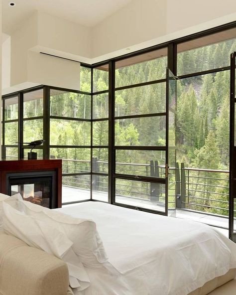 Steel window glass wall in this master bedroom with views of the forest and mountain and a cozy modern fireplace. #modernbedroom #bedroomdesign #windowdesign #glasswall #moderninterior #realtordotcom #contemporarydesign Bedroom Window Design, Glass Wall Design, Modern Glass House, Glass Room, House Outside Design, Bedroom Windows, Modern Fireplace, Window Glass, Rustic Bedroom