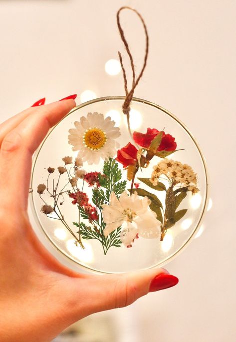 this resin ornament was made by hand with a bunch of real pressed flowers! it could be an ornament for your tree, or a suncatcher to hang in your window year round. makes a cute housewarming gift! measures 3 inches across, 0.5 inch deep. loop made with twine. *each piece i make is unique and made with different flowers! product may differ slightly from picture* Things To Make With Pressed Flowers, Dried Flower Ornament Diy, Pressed Flower Ornaments, Pressed Flower Art Projects, Pressed Flowers Ideas, Pressed Flower Gifts, Pressed Flower Christmas, Flowers Resin Art, Resin Gift Ideas