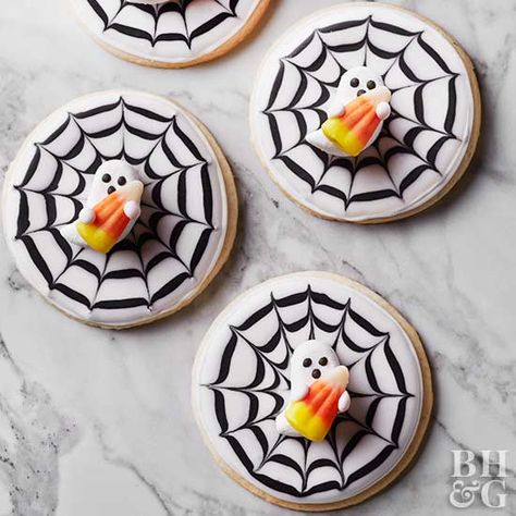 You won't believe how easy it is to decorate adorable Halloween cookies! To get this spooky spiderweb look, frost a round sugar cookie in white icing, and add concentric circles in black frosting. While both frosting colors are still wet, drag a toothpick from the center of the cookie toward the edge, and repeat all the way around the circles to complete the web. Top off with a ghost candy and a candy corn! Halloween Cookie Tip: Store decorated Halloween cookies in an airtight container at room Spooky Cookies, Halloween Sugar Cookies Decorated, Easy Halloween Cookies, Halloween Food Cupcakes, Spiderweb Design, Recetas Halloween, Halloween Cookie Recipes, Halloween Cookies Decorated, Halloween Sugar Cookies