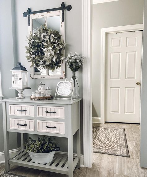 A six-paneled door is visible in this home's entryway where a geometric rug covers the gray floorboards. A rustic paneled mirror is decorated with a wreath above a gray and white console table bearing white ornaments. Grey Floorboards, Paneled Mirror, Barn Door Mirror, Gray Entryway, White Interior Door, White Kitchen Cupboards, White Interior Doors, Foyer Ideas, White Console Table