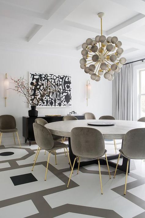 Contemporary white, gray, and black dining room boasts a large, round, gray dining table seating gray velvet dining chairs with gold legs on a white and gray painted wood floor. Gold Dining Room, Grande Table A Manger, Round Dining Room Sets, Grey Dining Tables, Round Dining Room Table, Grey Dining Room, Dining Room Contemporary, Round Dining Room, Black Dining