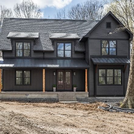 A charcoal farmhouse with black roof. Brown double doors with greenery and rug. Black light fixtures on sides of double doors. Photography by The Home Aesthetic & Builder Josh Loewen. Black Gray House Exterior, Dark Gray Siding With Black Metal Roof, Black House Gray Roof, Black Roof Siding Colors, Black Siding Black Roof, Inkwell Exterior Paint, Charcoal Exterior House Colors Farmhouse, Charcoal Gray Exterior House, Charcoal Siding Black Windows