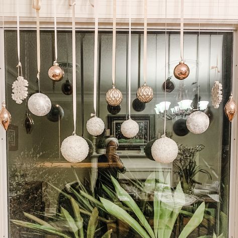 Ornaments Hanging From Window, Ornaments On Window, Hanging Baubles Window, Bauble Window Display, Ornaments On Ribbon In Window, Shop Ornament Display, Christmas Balls Window Display, Christmas Ornament Window Decorations, Easy Christmas Window Display