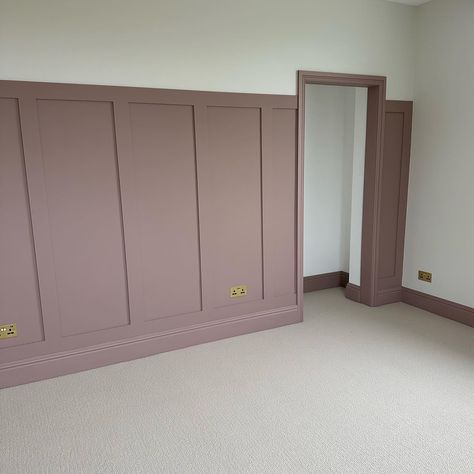 A neutral, textured carpet, paired with panelling and skirting boards painted in a muted, dusky pink tone. The image features traditional style radiators painted in a glossy white shade.