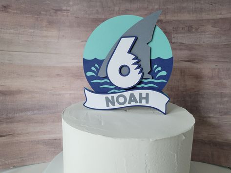 "Shark cake topper This cake topper will make a splash on your cake. It is the fun addition to your shark themed birthday party. What is included in your purchase:  This listing is for the Shark cake topper only.  Coordinating décor can be found in my shop  If you would like other coordinating décor, please message me and I would be glad to help. Details: -  This topper is single sided; meaning the back is NOT decorated and is simply a solid color back. - Cake topper is approx. 5\" wide x 5.5\" tall  - All cake toppers come attached on a round clear plastic lollipop stick 8\" long. Total cake topper heights vary by design. Customization: - Please include the name and age in the Notes to Seller section.  - Colors: navy, sky blue, gray, white. Colors can be customized. Due to all the fact th Ocean Cake Topper, Under The Sea Cake Topper, Sea Cake Topper, Shark Cake Topper, Ocean Cake, Under The Sea Cake, Shark Party Decorations, Sea Cake, Ocean Birthday Party