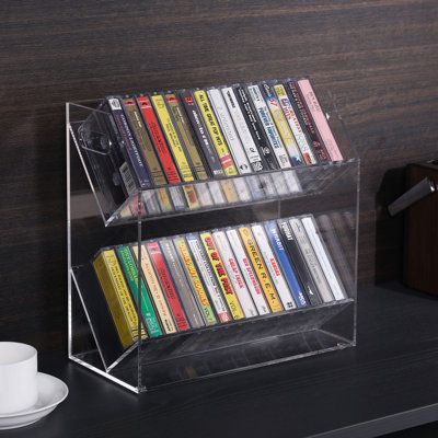 Showcase your retro cassette tapes while keeping up to 30 cases neatly stored in this clear acrylic tape holder display rack. Ideal for your home, office or music studio, this tiered clear acrylic cassette tape storage case has two cutout handles to let you transport your tapes when needed. Two angled tiers allow a large quantity of retro cassette tapes to be easily viewed and selected when listening to your music collection. It will perfectly complement the various style of home decor. | Latitu Cassette Tape Holder, Music Display, Media Shelves, Cassette Storage, Cassette Tape Storage, Media Shelf, Tabletop Design, Tape Storage, Vinyl Aesthetic