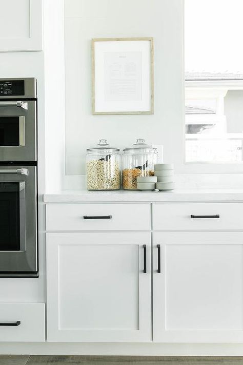 White shaker kitchen cabinets contrasted with long oil rubbed bronze pulls are fitted beneath a window. Oiled Bronze Hardware, Small Kitchen Plans, Taupe Kitchen, White Shaker Kitchen Cabinets, Bronze Pulls, White Shaker Kitchen, Cabinets Storage, Kitchen Finishes, Shaker Kitchen Cabinets