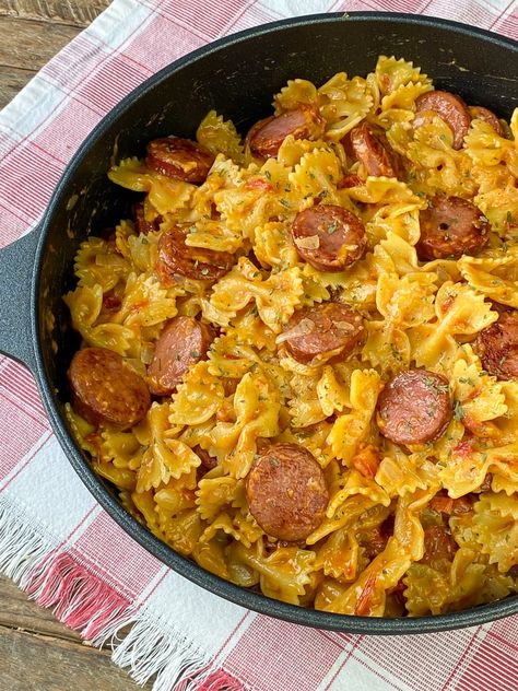 Tender cooked bow tie pasta with a creamy sauce made from whipping cream, diced tomatoes and cheddar cheese with pieces of sausage generously spread around and cajun seasoning accenting the one skillet meal on a red and white plaid napkin. Cajun Pasta With Sausage, Sausage Crostini, Sausage Pasta Dinner, Bow Tie Pasta Recipe, Cajun Sausage Pasta, Sausage Pasta Recipe, Smoked Sausage Pasta, Cajun Sausage, Smoked Sausage Recipes