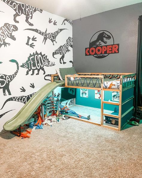 Surprise your son with a fun Jurassic World-themed bedroom. The adorable tiny bunk bed with olive sheets features a slide attached to its side. Complete the space with two dinosaur-themed accent walls. Dinosaur Room Ideas Toddler, Kids Dinosaur Bed, Small Dinosaur Bedroom Ideas, Dino Inspired Bedroom, Toddler Boy Room Decor Dinosaur, Dinosaur Boy Room Ideas, Jurassic World Room Decor, Big Boy Dinosaur Bedroom, Dinosaur Bedroom Ideas For Boys