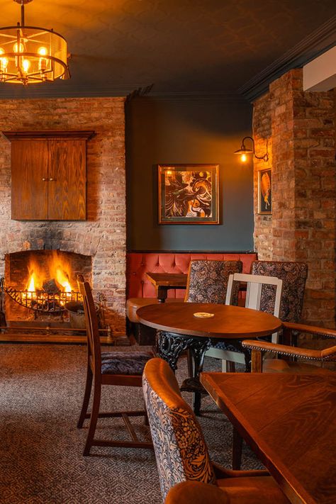 warm/dull lit room, burnt orange seating area with burning fire place creating a cosy environment, deep wooden tables with a glossy finish. detailed patterned chairs. Country Pub Interior Design, Pub Lighting Ideas, Pub Design Interiors, Bar Interior Design Pub, Pub Bar Design, Country Pub Interior, English Pub Interior, Pub Fireplace, English Pub Decor