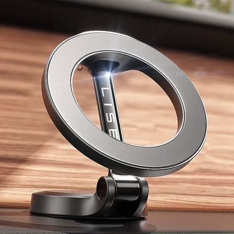 The photo shows a silver, steel alloy circular phone mount that uses MagSafe technology to hold the device in place.  It shows the mount set up on a flat surface with a wood panel behind it. Iphone Car Holder, Car Cell Phone Holder, Magnetic Phone Holder, Support Telephone, Latest Iphone, Car Holder, Phone Mount, Cell Phone Holder, Car Phone Holder