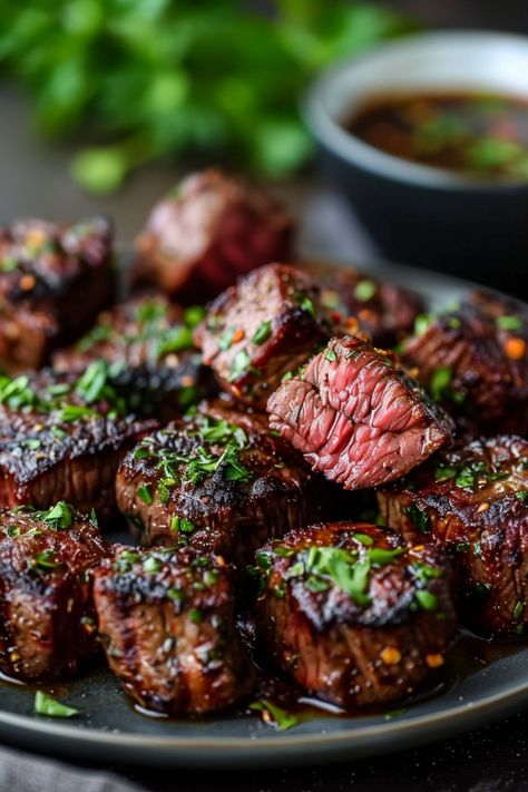 Grilled beef steak bites garnished with herbs on a plate, with a bowl of dipping sauce in the background. Air Fryer Steak Kebab Recipes, Air Fryer Teriyaki Steak Bites, Ribeye Steak Bites In Air Fryer, Steak Bites On The Grill, Air Fryer Steak Tips Recipe, Healthy Air Fryer Steak Bites, Shell Steak Recipes, Steak Bits In Air Fryer, Air Fry Garlic Butter Steak Bites