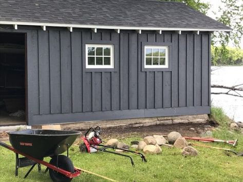 Board and batten siding using dark gray stained cedar boards on boathouse. Grey Vertical Siding Exterior, Board And Batten Siding With White Windows, Wood Board And Batten Exterior, Board And Batten Siding Black, Grey Board And Batten Exterior, Nice Garage, Stained Cedar, Black Shed, Diy Board And Batten