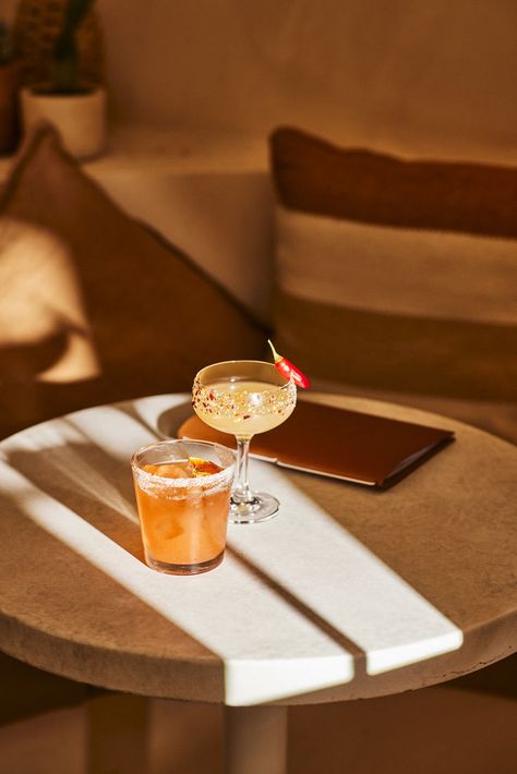 Cocktail photography of two margaritas upon a circular marble table in a Mexican themed bar. A short orange cocktail sits in a tumbler, with a salted rim. A chilli margarita in tall coup glass, decorated with salt, chilli flakes and a whole red chilli. Image belongs to Instant Crush Creative. Cocktail Photography Creative, Chilli Margarita, Orange Cocktail, Orange Cocktails, Cocktail Photography, Drink Photography, Chilli Flakes, Red Chilli, Marble Table